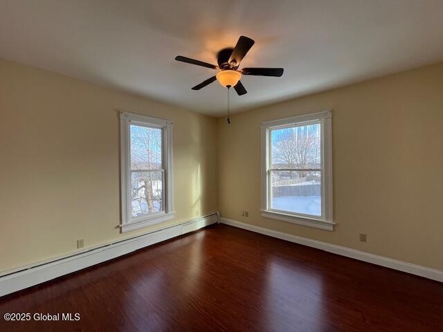 empty room featuring dark wood-type flooring, ceiling fan, and a baseboard radiator