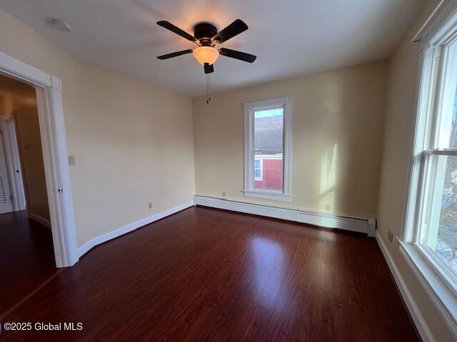 empty room featuring ceiling fan, dark hardwood / wood-style floors, and a baseboard heating unit