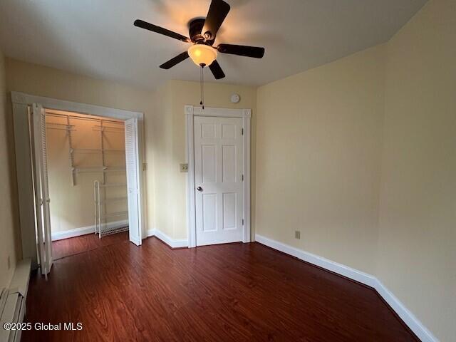 unfurnished bedroom with ceiling fan, a baseboard radiator, a closet, and dark hardwood / wood-style floors