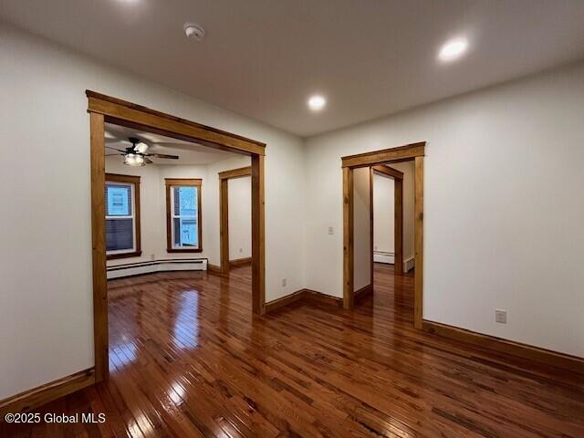 empty room featuring baseboard heating, ceiling fan, and dark hardwood / wood-style floors