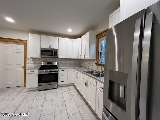 kitchen featuring white cabinets, appliances with stainless steel finishes, decorative backsplash, and sink