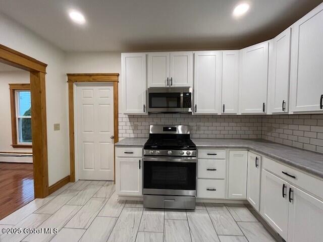 kitchen featuring backsplash, stainless steel appliances, a baseboard radiator, and white cabinets