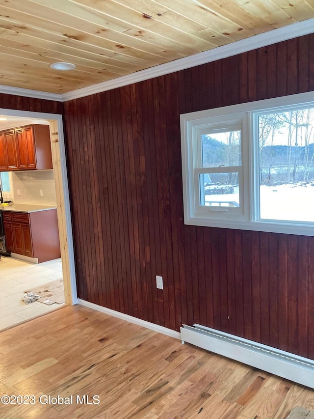 interior space with ornamental molding, baseboard heating, light hardwood / wood-style floors, and wooden walls