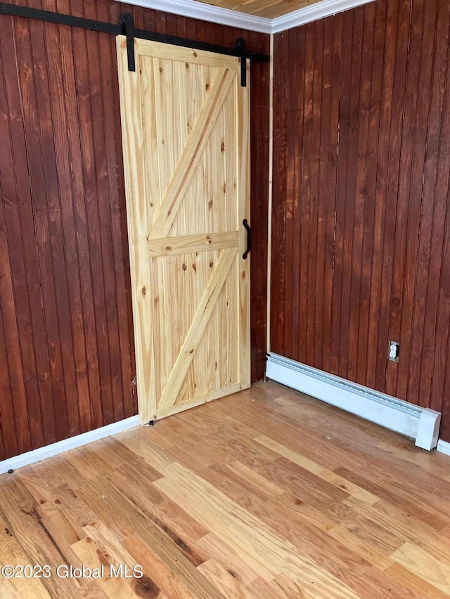 unfurnished room featuring wood walls, baseboard heating, light hardwood / wood-style floors, and a barn door