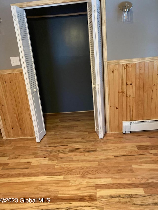 corridor with a baseboard heating unit, wooden walls, and light hardwood / wood-style flooring