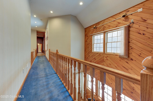 hallway with vaulted ceiling, wood walls, and carpet flooring