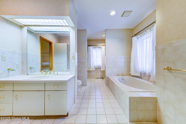 bathroom with toilet, tile walls, tile patterned floors, tiled tub, and vanity