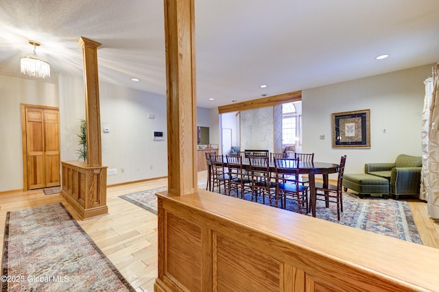 dining area featuring decorative columns, light wood-type flooring, and an inviting chandelier