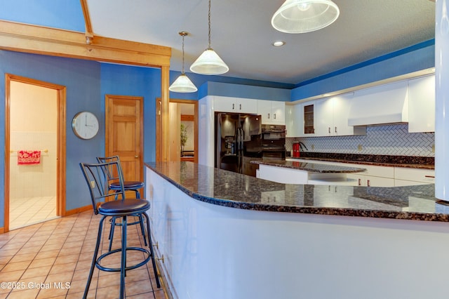 kitchen featuring light tile patterned floors, black fridge, wall chimney exhaust hood, white cabinetry, and decorative light fixtures