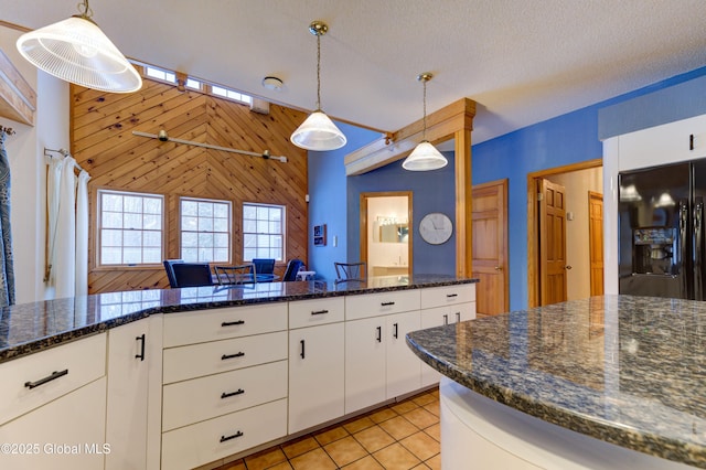 kitchen featuring black fridge with ice dispenser, decorative light fixtures, a textured ceiling, white cabinetry, and wood walls