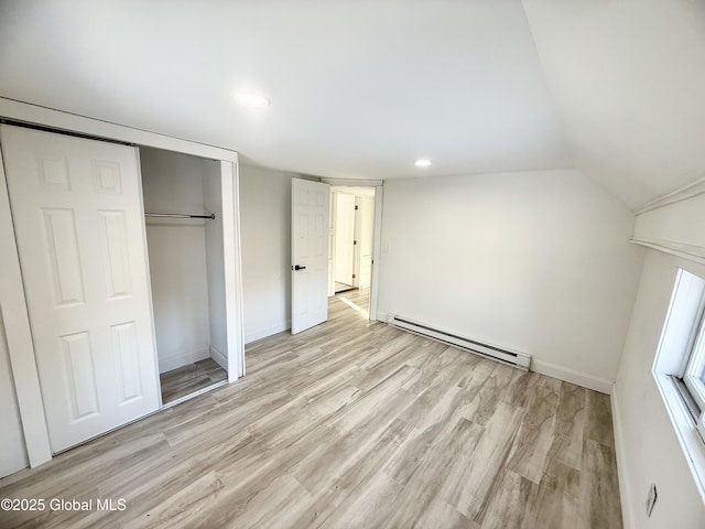 unfurnished bedroom featuring light hardwood / wood-style floors, a closet, baseboard heating, and vaulted ceiling