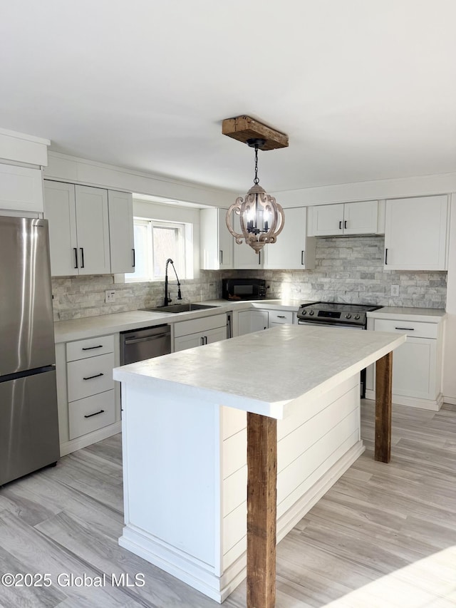 kitchen featuring stainless steel appliances, sink, white cabinets, a kitchen island, and pendant lighting