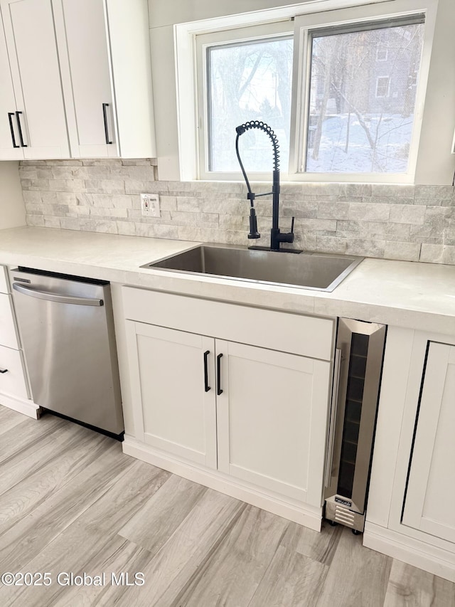 kitchen featuring wine cooler, light hardwood / wood-style floors, sink, white cabinetry, and stainless steel dishwasher