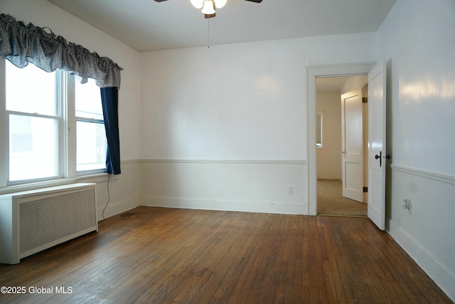 unfurnished room with ceiling fan, radiator heating unit, a healthy amount of sunlight, and dark wood-type flooring