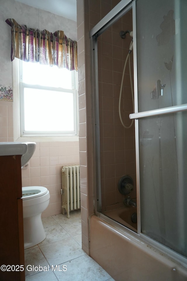 full bathroom with radiator heating unit, tile patterned flooring, tile walls, toilet, and shower / bath combination with glass door