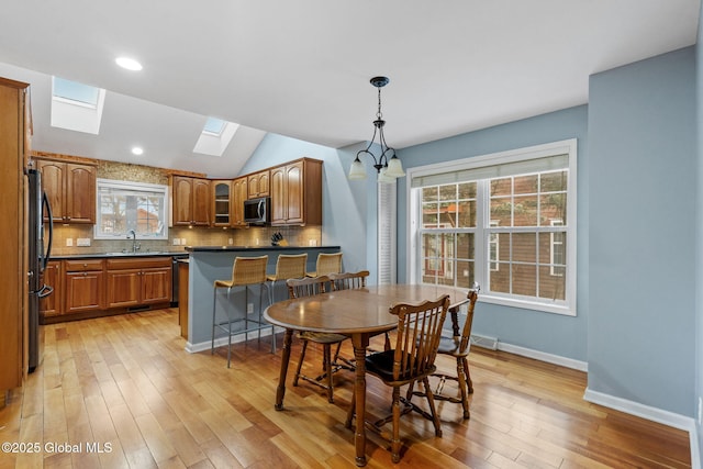 dining space with vaulted ceiling with skylight, light hardwood / wood-style flooring, and sink