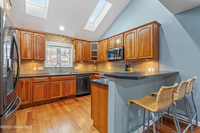 kitchen with vaulted ceiling with skylight, kitchen peninsula, sink, appliances with stainless steel finishes, and a kitchen breakfast bar