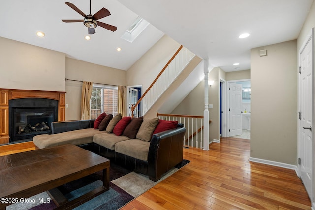 living room featuring ceiling fan, a skylight, light hardwood / wood-style flooring, and high vaulted ceiling