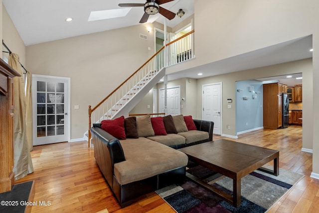 living room featuring high vaulted ceiling, a skylight, ceiling fan, and light wood-type flooring