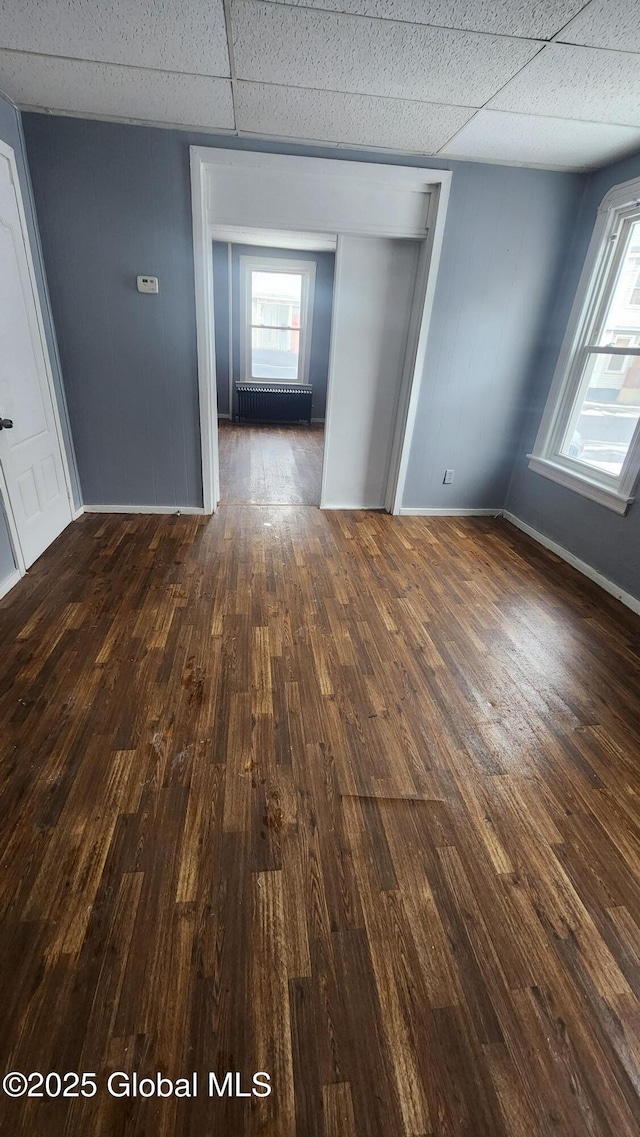 unfurnished room with a drop ceiling, dark hardwood / wood-style floors, and radiator