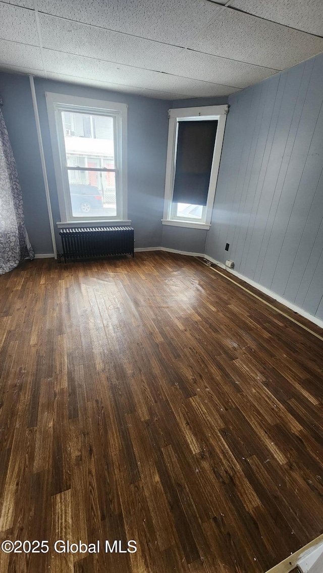 empty room featuring dark hardwood / wood-style floors, radiator, and wooden walls