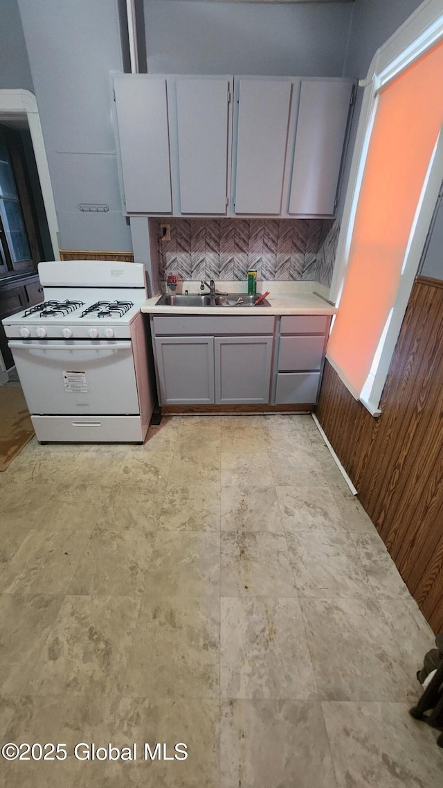 kitchen with tasteful backsplash, gray cabinets, white gas range oven, sink, and wooden walls