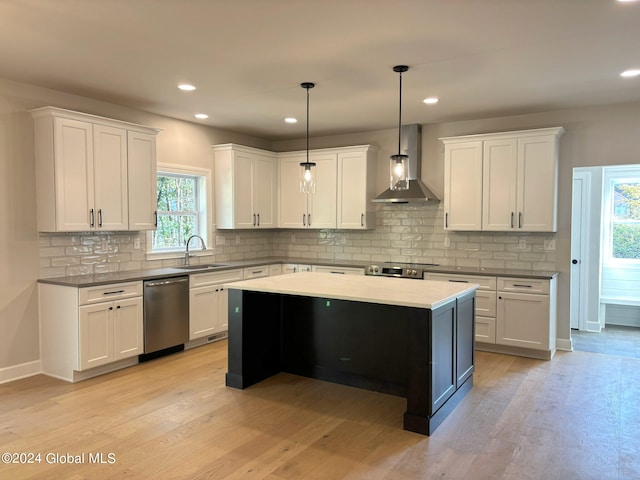 kitchen featuring white cabinetry, light hardwood / wood-style flooring, appliances with stainless steel finishes, pendant lighting, and wall chimney range hood