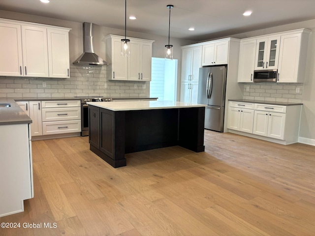 kitchen featuring appliances with stainless steel finishes, decorative light fixtures, a center island, wall chimney range hood, and light hardwood / wood-style flooring