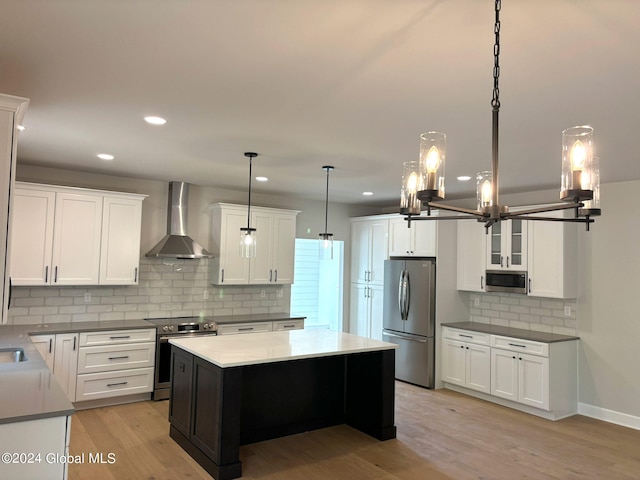 kitchen featuring appliances with stainless steel finishes, decorative light fixtures, white cabinetry, light wood-type flooring, and wall chimney exhaust hood