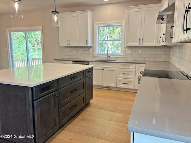 kitchen with decorative light fixtures, sink, white cabinets, a center island, and wall chimney exhaust hood