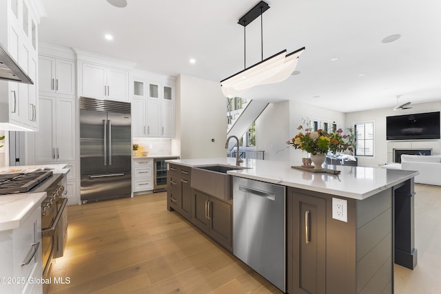 kitchen with sink, decorative light fixtures, white cabinets, high end appliances, and ventilation hood