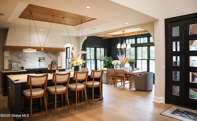 interior space featuring hanging light fixtures, a notable chandelier, light hardwood / wood-style floors, decorative backsplash, and a tray ceiling