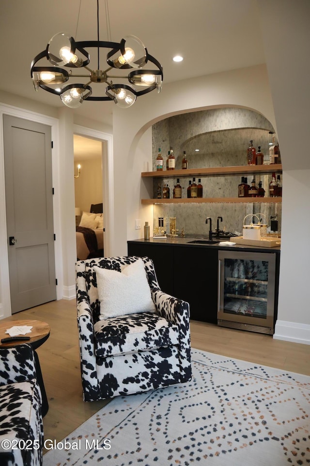 bar with wine cooler, a notable chandelier, pendant lighting, sink, and light hardwood / wood-style flooring