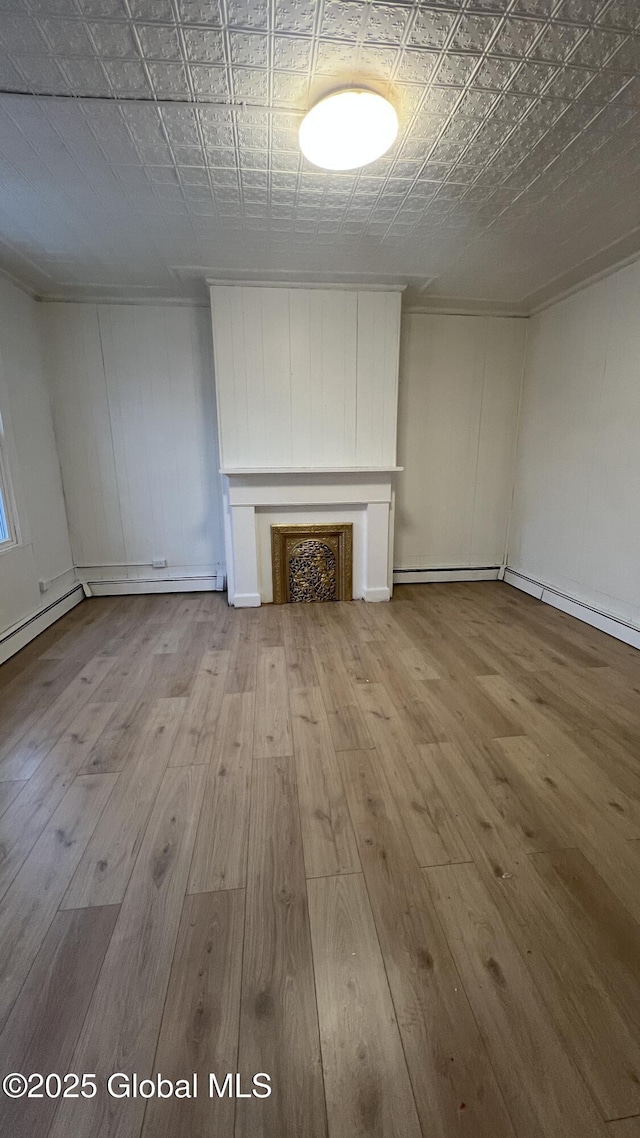 unfurnished living room featuring a baseboard heating unit, a fireplace, and light wood-type flooring