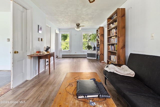 living room featuring baseboard heating, a textured ceiling, ceiling fan, and wood-type flooring