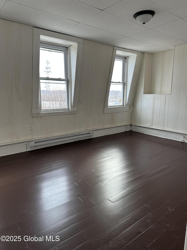 spare room with a drop ceiling, dark hardwood / wood-style floors, and wooden walls