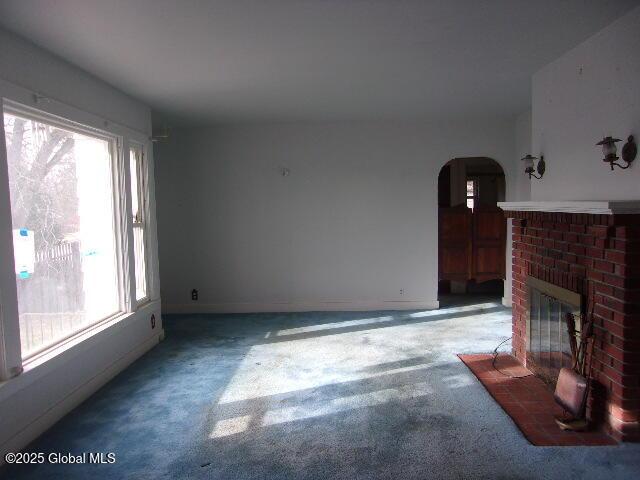 unfurnished living room with a brick fireplace, carpet floors, and a wealth of natural light