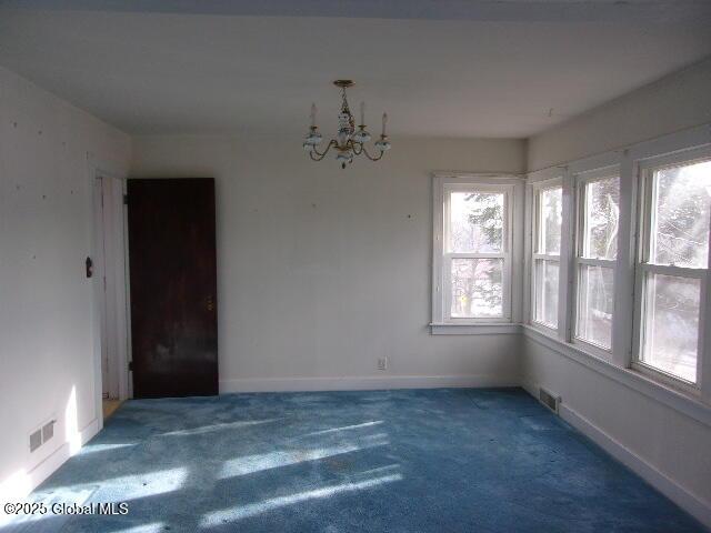 carpeted empty room with an inviting chandelier