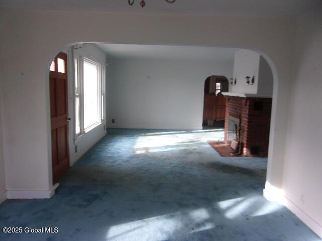 unfurnished living room featuring a brick fireplace and dark carpet