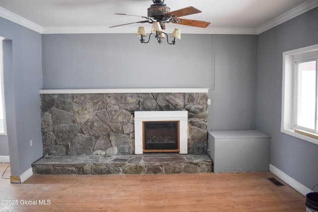 unfurnished living room with ceiling fan, a stone fireplace, ornamental molding, and hardwood / wood-style flooring