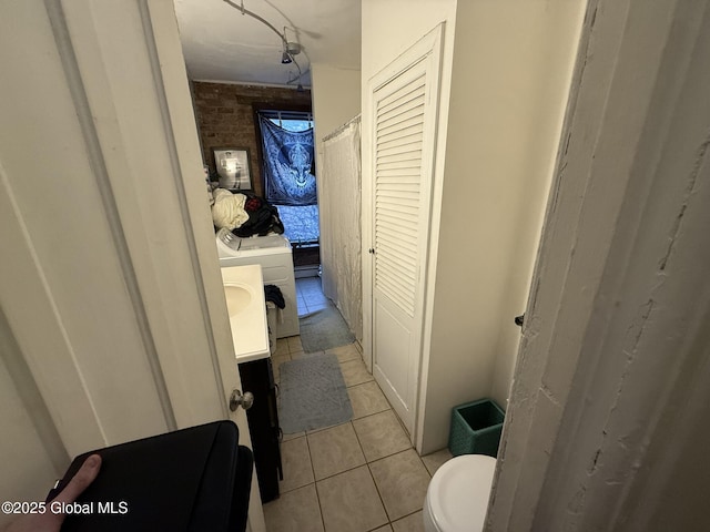 bathroom with brick wall, washer / dryer, tile patterned floors, vanity, and toilet