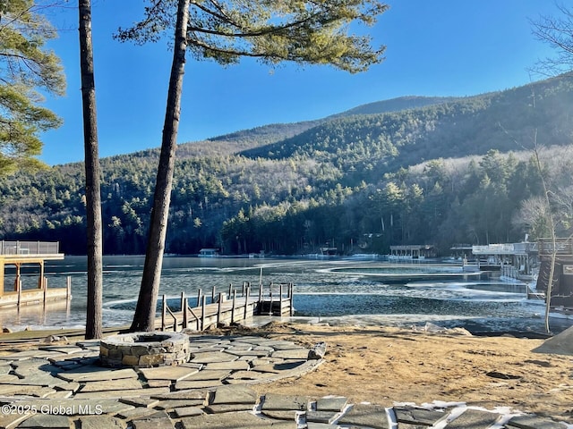 view of water feature with a boat dock, a wooded view, and a mountain view