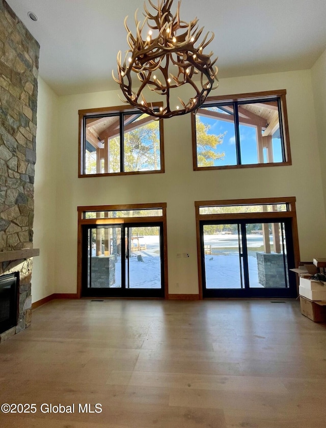 unfurnished living room featuring a towering ceiling, baseboards, wood finished floors, and a stone fireplace