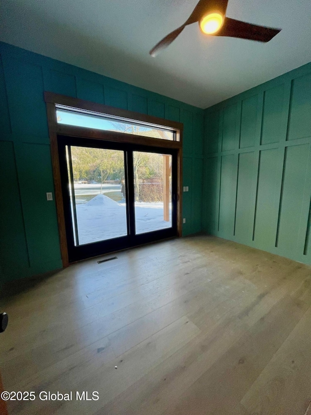 empty room featuring visible vents, a decorative wall, light wood-style flooring, and ceiling fan