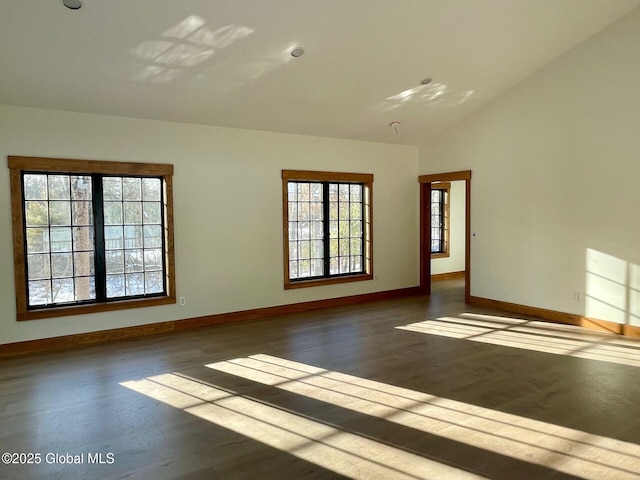 empty room featuring dark wood-style floors, vaulted ceiling, and baseboards