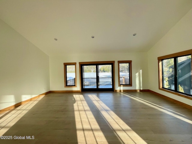 spare room with vaulted ceiling, plenty of natural light, baseboards, and wood finished floors