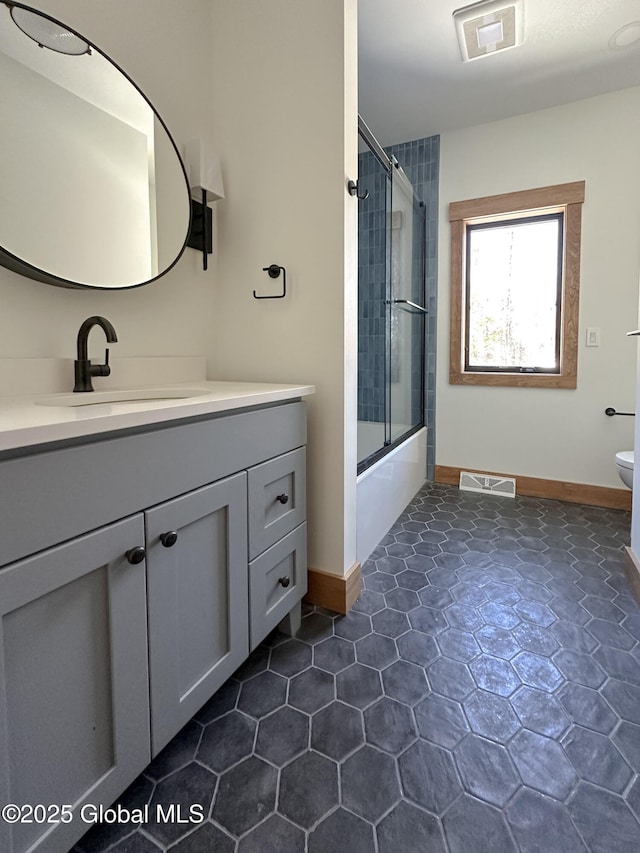 full bath with visible vents, toilet, combined bath / shower with glass door, vanity, and baseboards