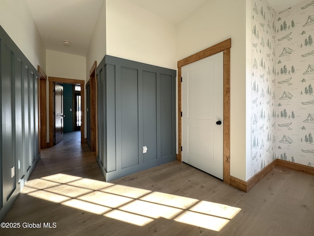 interior space featuring wallpapered walls, a decorative wall, baseboards, and wood finished floors