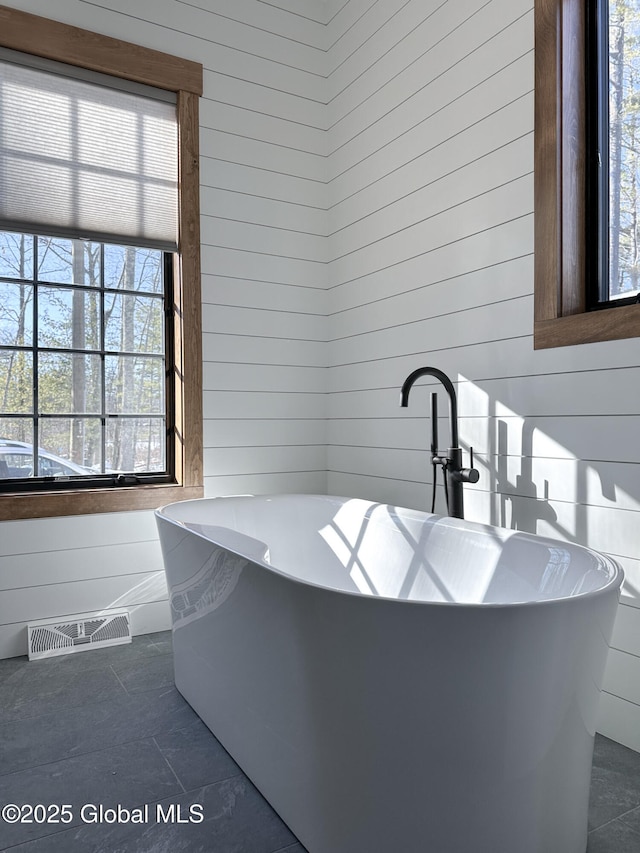 bathroom with visible vents, a freestanding bath, and wooden walls