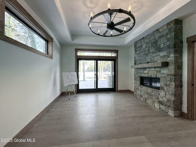 unfurnished living room featuring baseboards, a stone fireplace, a tray ceiling, and light wood-style floors